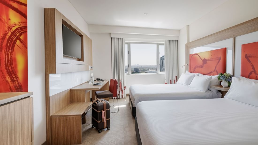 TV and work desk by the beds in Superior Room with vibrant orange artworks & a city view at Novotel Sydney Olympic Park