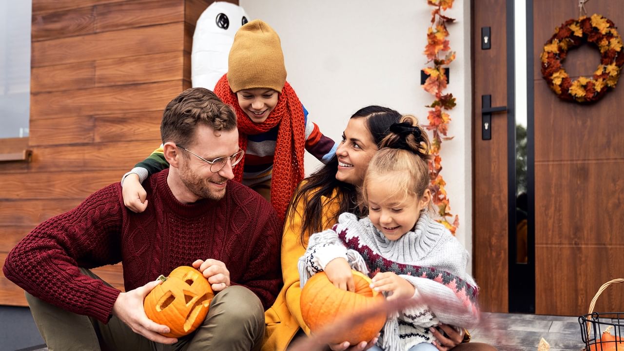 Family of four smiling and enjoying Halloween pumpkin carving together