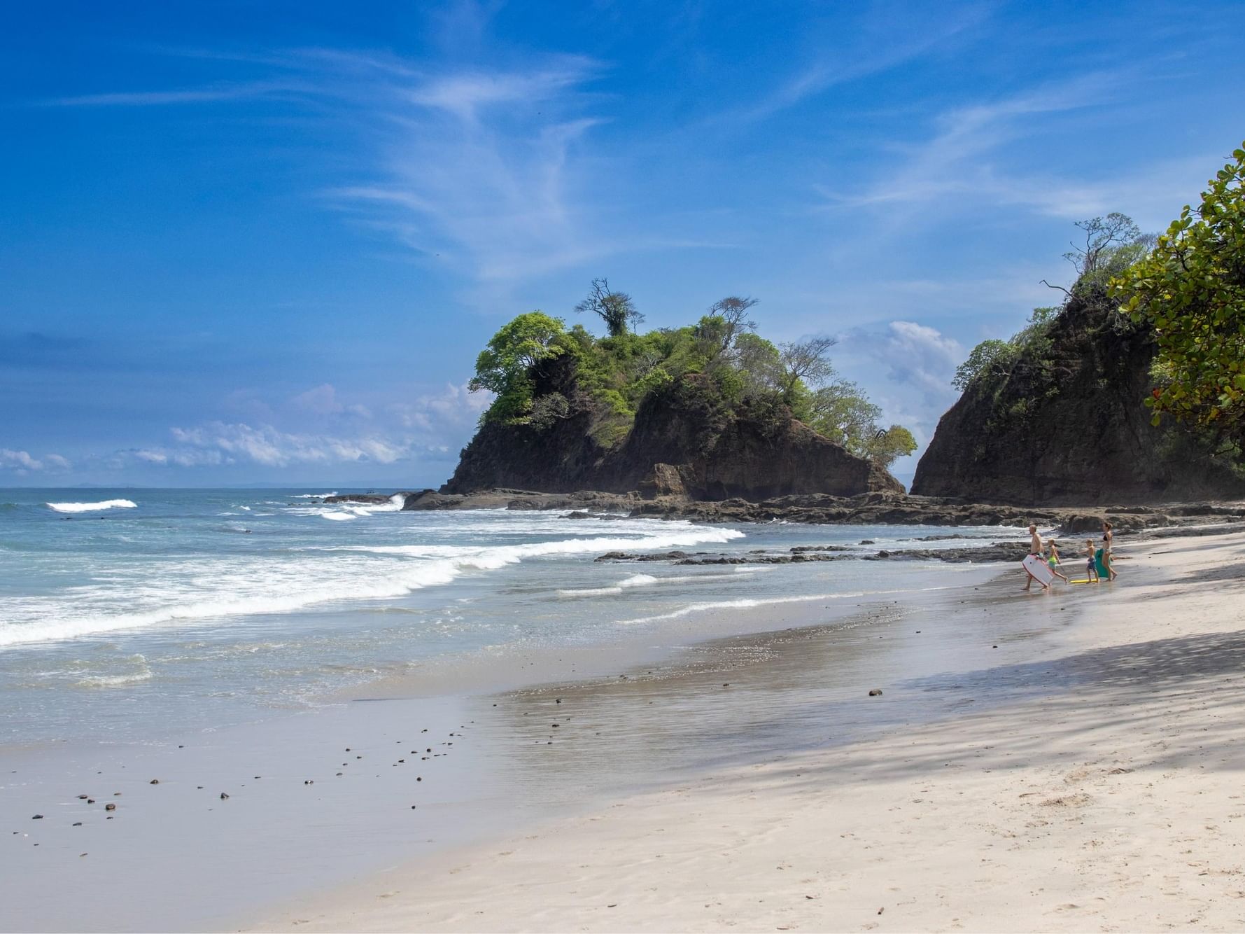 Sandy beach with ocean waves and rocky cliffs showcasing Punta Esmeralda by Punta Leona.