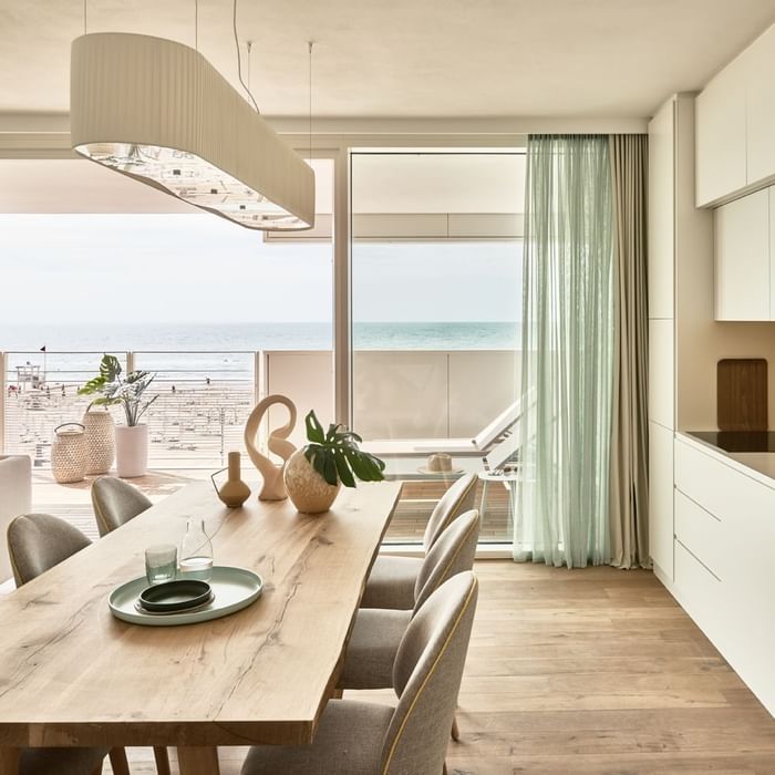 Modern dining area with a wooden table, stylish chairs, and ocean view through large windows at Falkensteiner Hotels