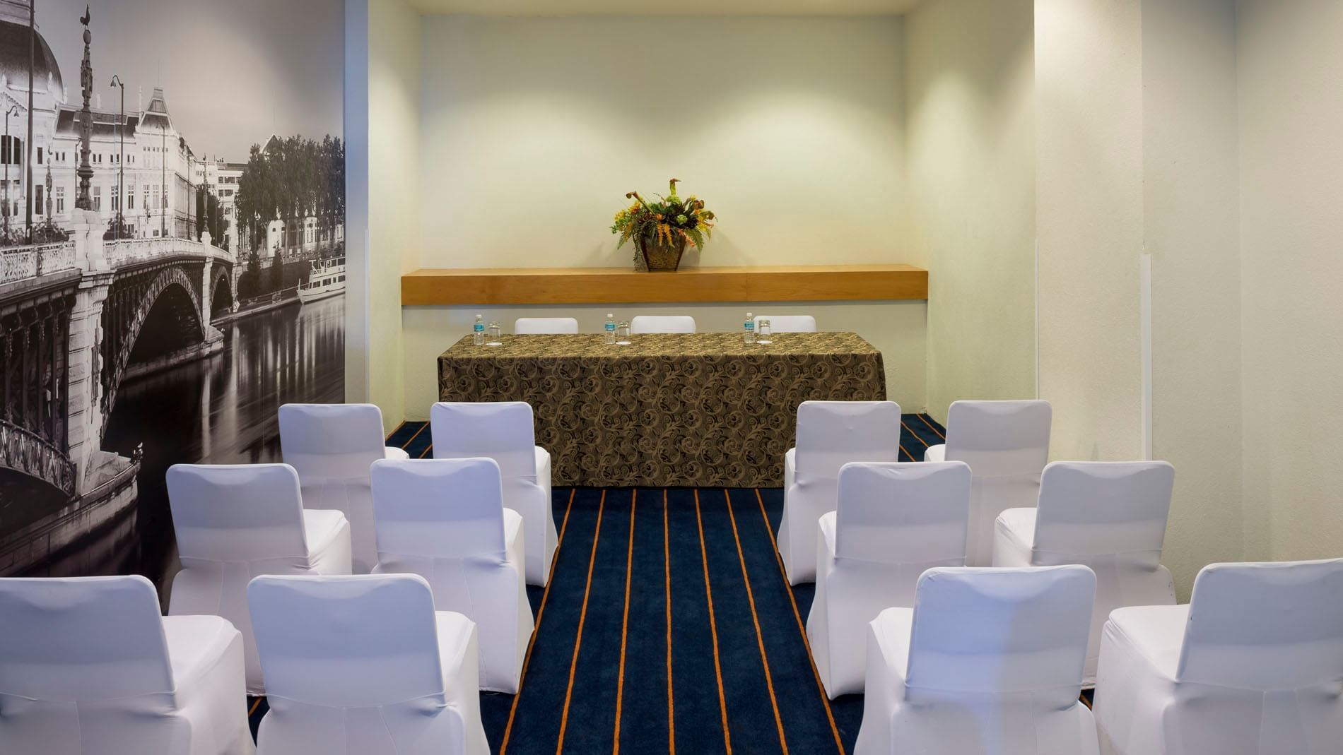 Intimate theater-style meeting room with a city mural and white chair covers at Real Inn Nuevo Laredo