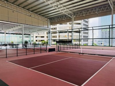 Pickleball court at One World Hotel, with a dark red surface and black nets, under a high, open roof structure