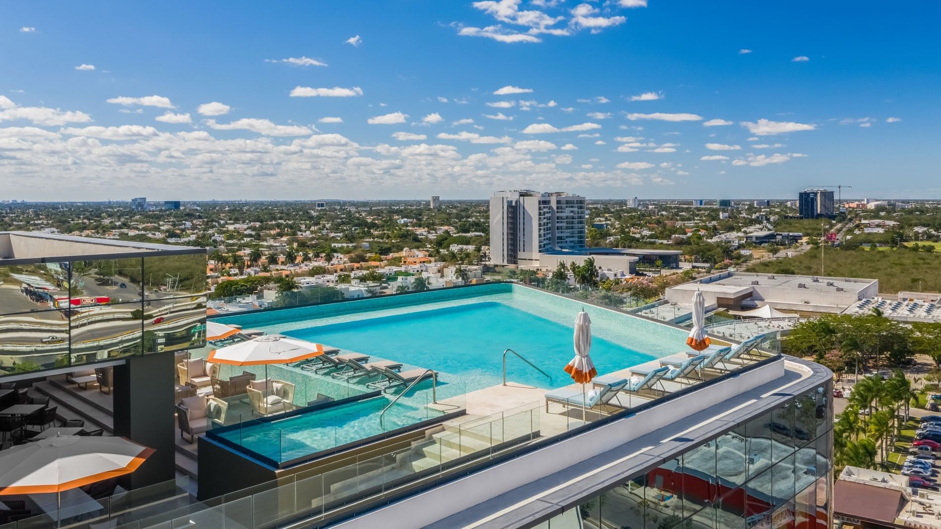 Spacious rooftop deck showcasing a sparkling pool, white umbrellas, and blue skies at Camino Real Merida