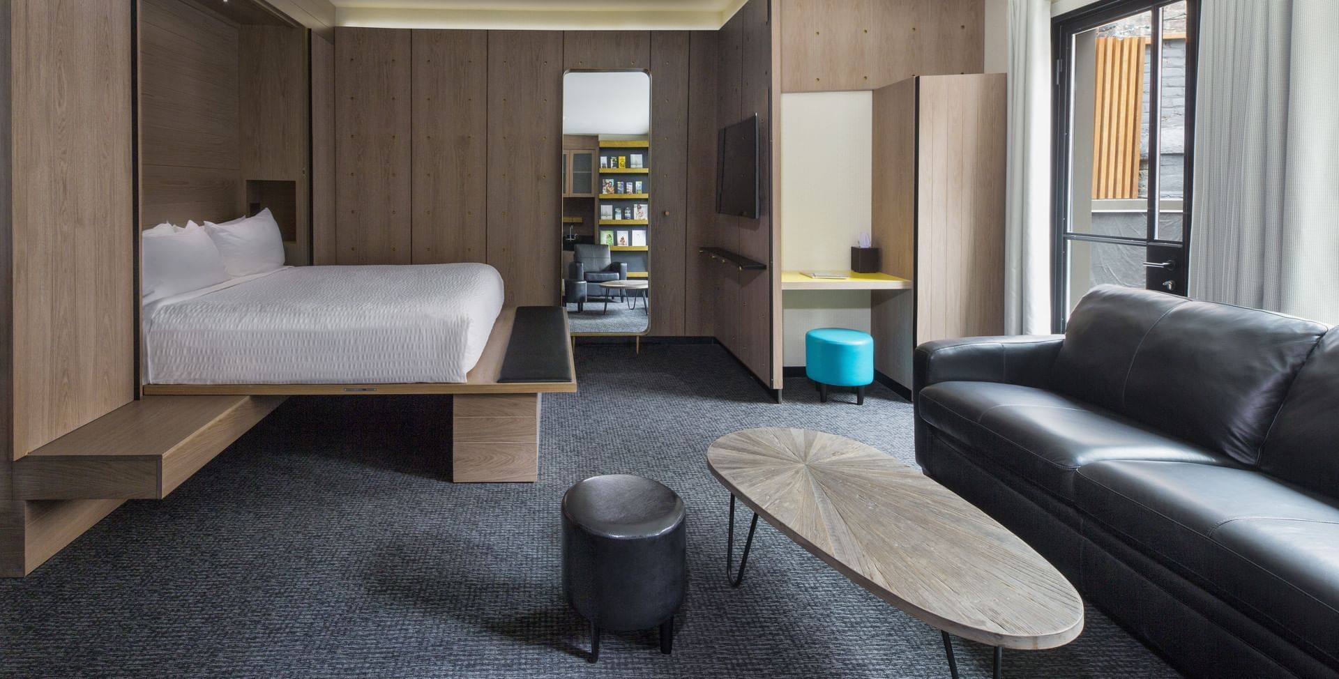 A wide-angle view of a hotel room with a bed, sofa, coffee table, and wood paneling on the walls.