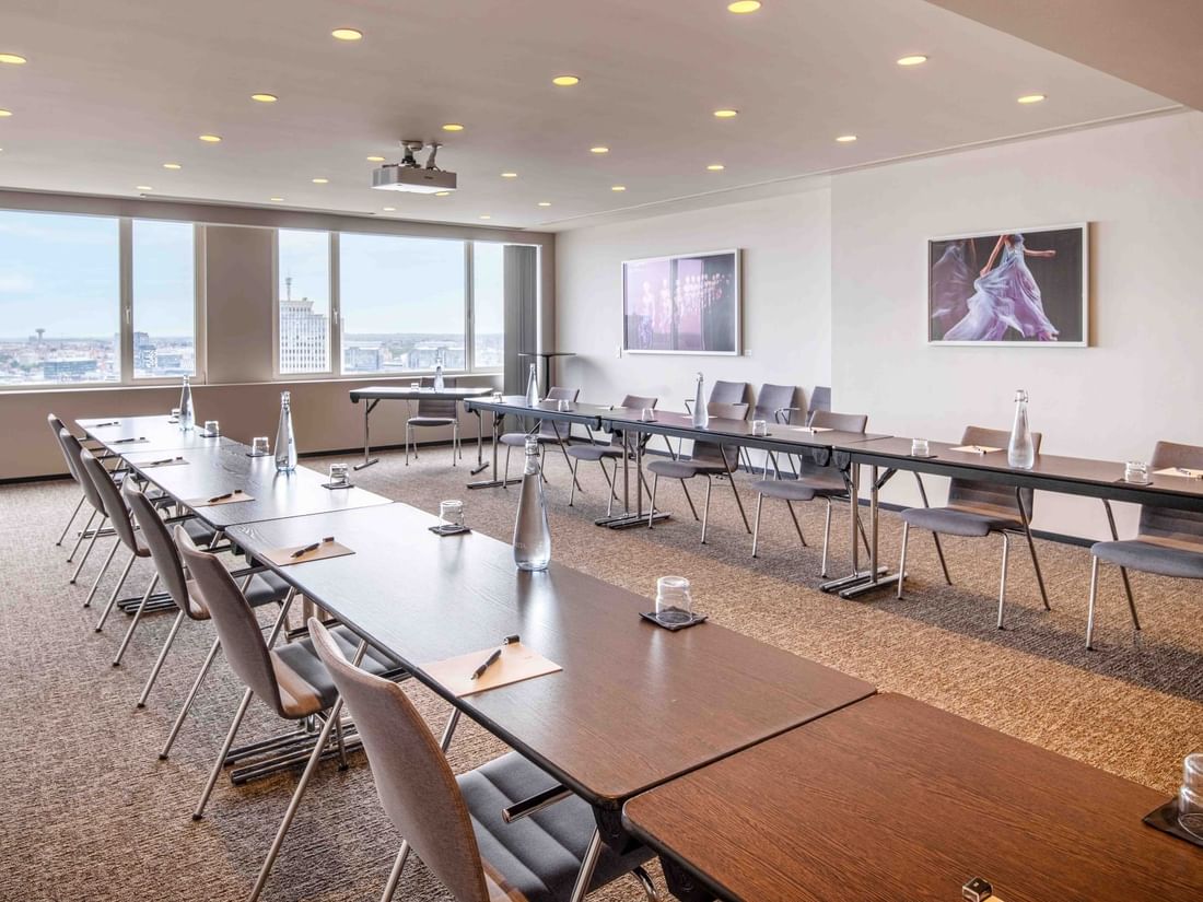 Meet 26 one meeting room with long tables, chairs, and large windows overlooking a city at The Hotel Brussels