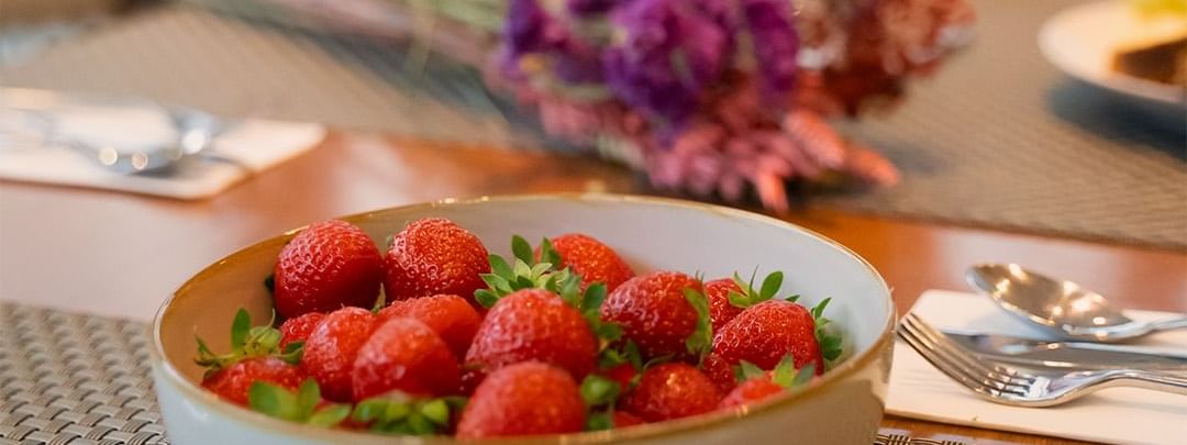 Bowl of red strawberries and utensils on a dining table at Warwick Hotels and Resorts, with blurred flowers in the background
