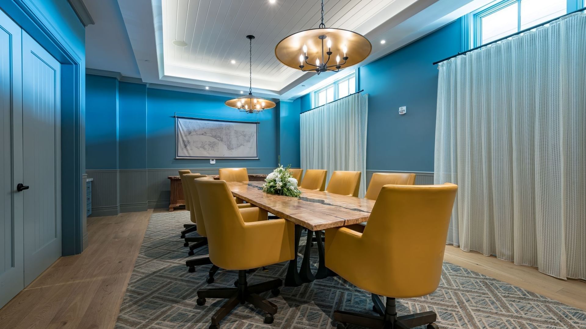 Boardroom with blue walls, wooden table, yellow chairs, and pendant lighting at Camp Creek Inn in Inlet Beach.