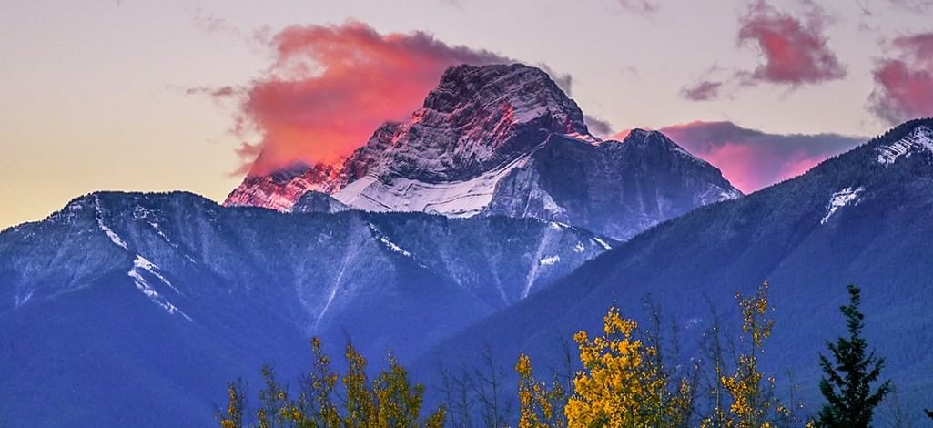 Sunset over snow-capped mountain peak near Canmore, Alberta with vibrant pink clouds and autumn trees in foreground