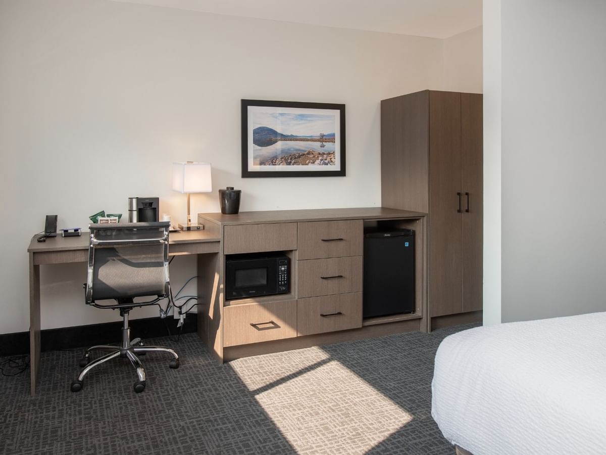Hotel room with desk, chair, microwave, refrigerator, cabinet, picture frame, and bed.