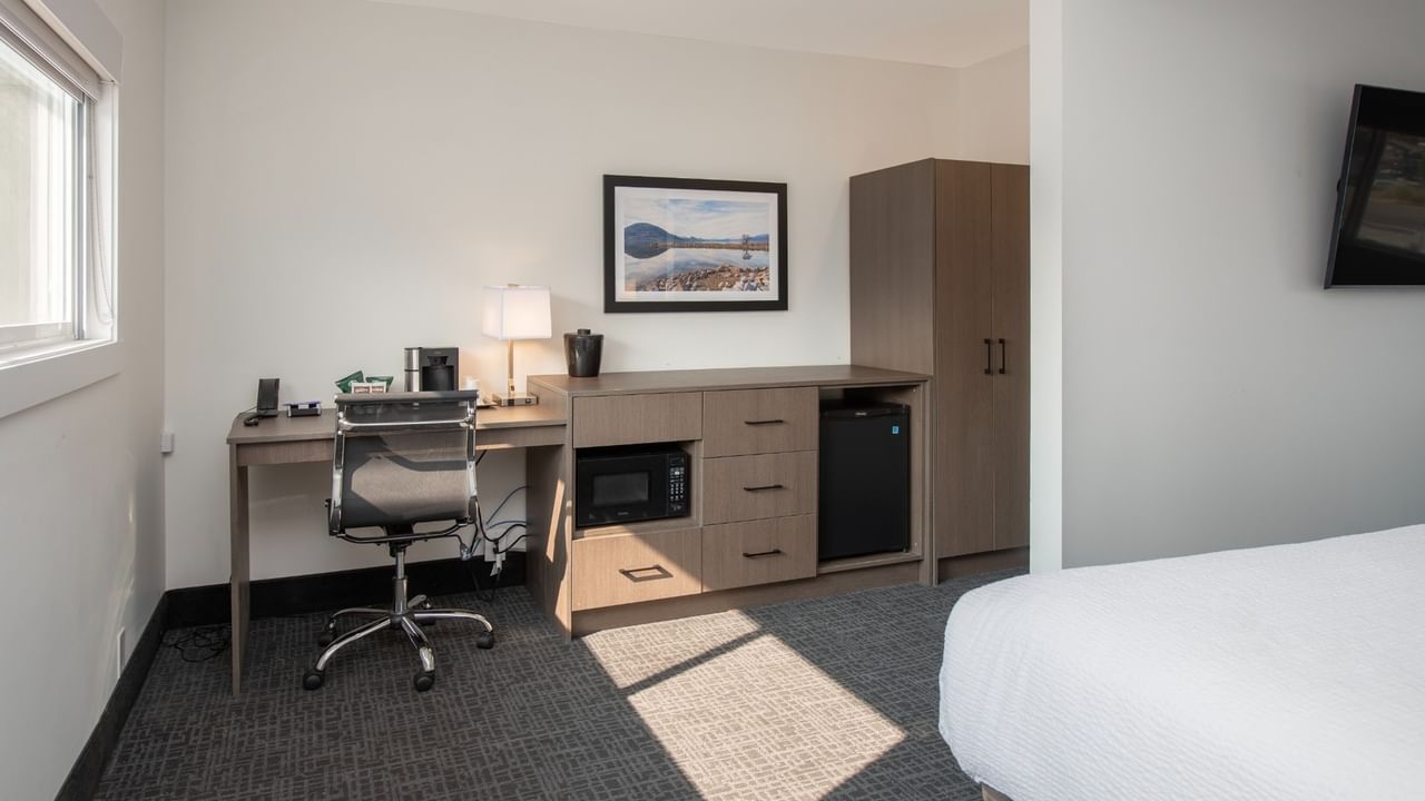 Hotel room with desk, chair, microwave, refrigerator, cabinet, picture frame, and bed.