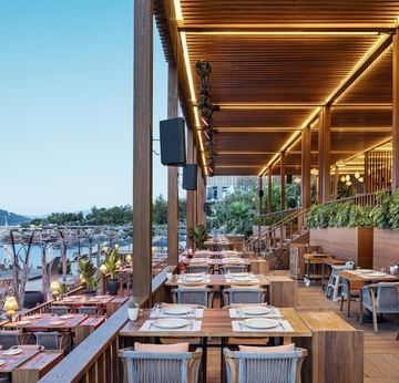 Beef Burger House with wooden tables, cushioned chairs, and a stunning view of the sea at Titanic Luxury Collection Bodrum