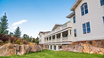 A side view of the white Aspire Residences at The Stanley Hotel, with large rocks and green grass in the foreground