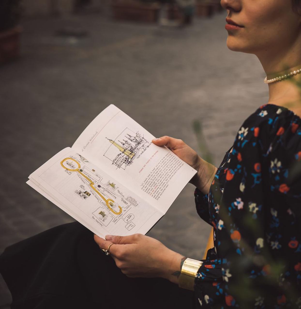 Woman sitting on a bench while holding a book in outside at Rome Luxury Suites