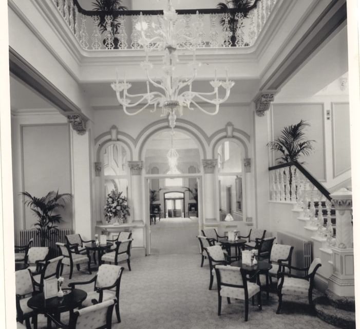 Black and white photo of a grand white marble lobby with a huge chandelier and cafe tables at The Milner York