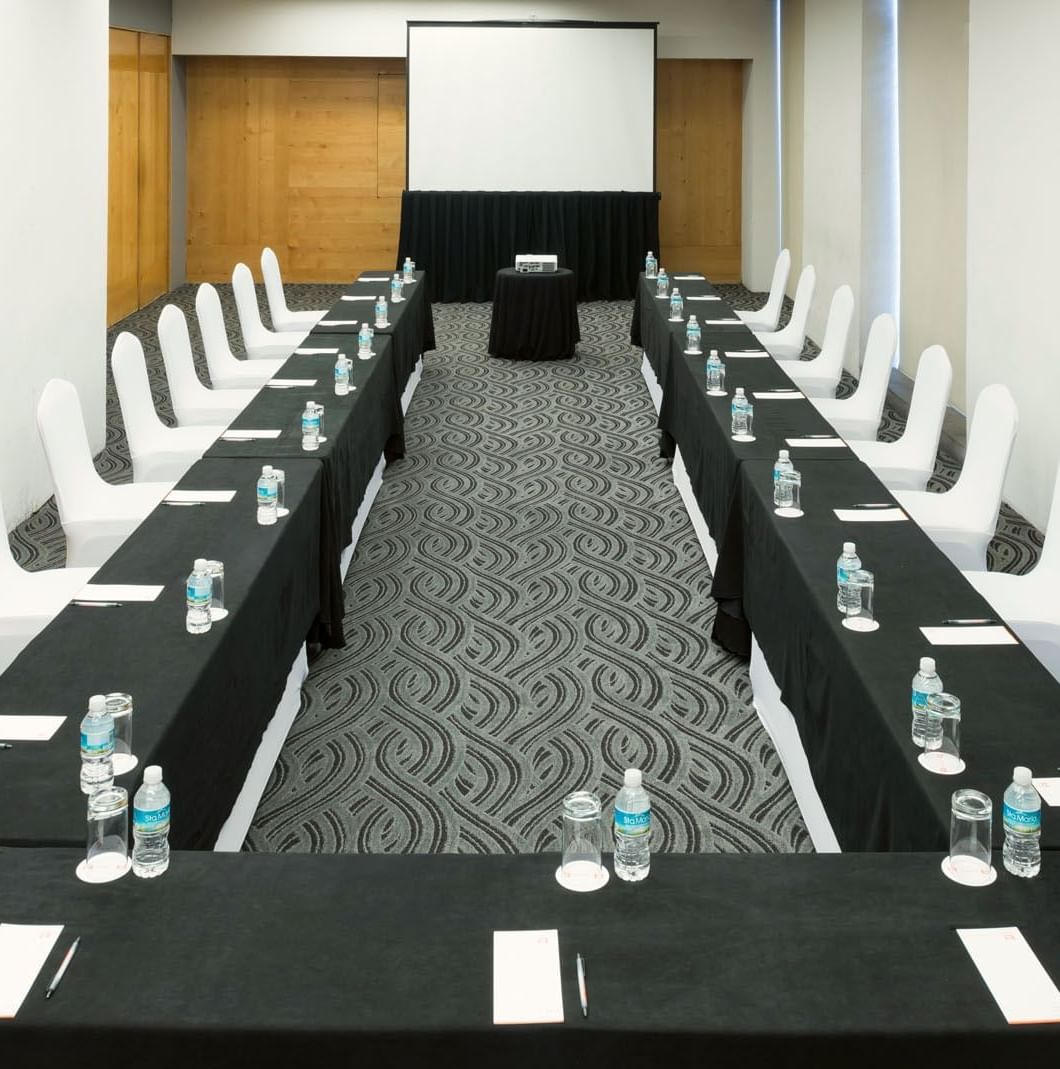 U-shaped Mexico Venue with black linens, white chairs, and a large projector screen at Real Inn Perinorte