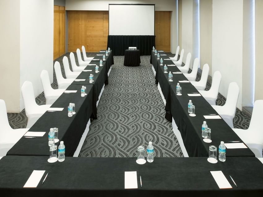 U-shaped Mexico Venue with black linens, white chairs, and a projector screen at Real Inn Perinorte