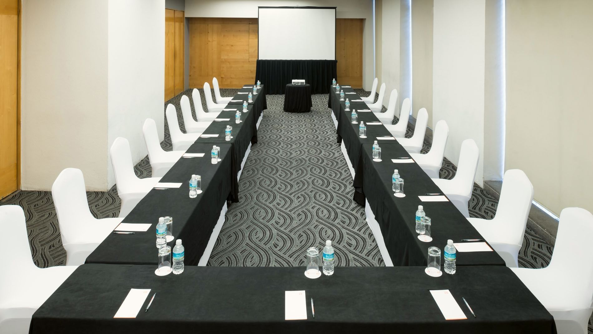 U-shaped Mexico Venue with black linens, white chairs, and a projector screen at Real Inn Perinorte