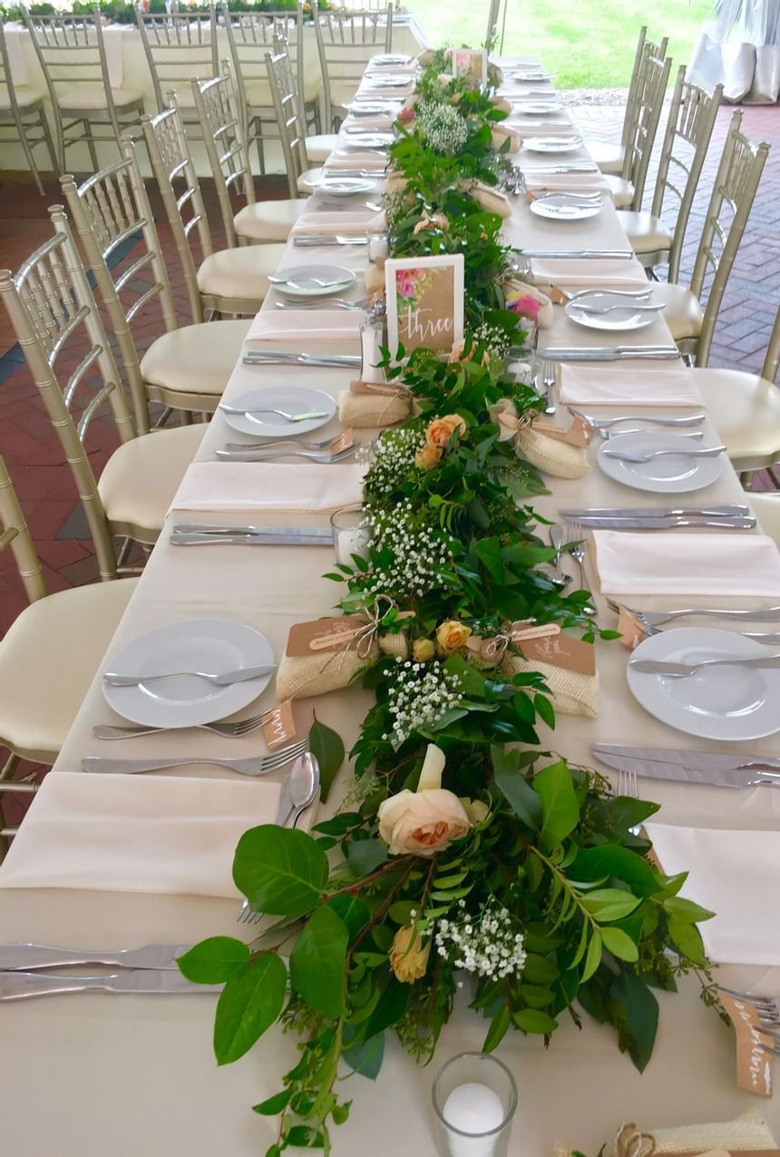 Long banquet table with white linens, gold chiavari chairs, and garland centerpiece at Aramark Chauncey Conference Center