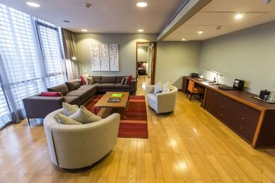 Sala de estar con sofá junto a escritorio y sillas bajo luz suave en Executive Suite de NOI Vitacura