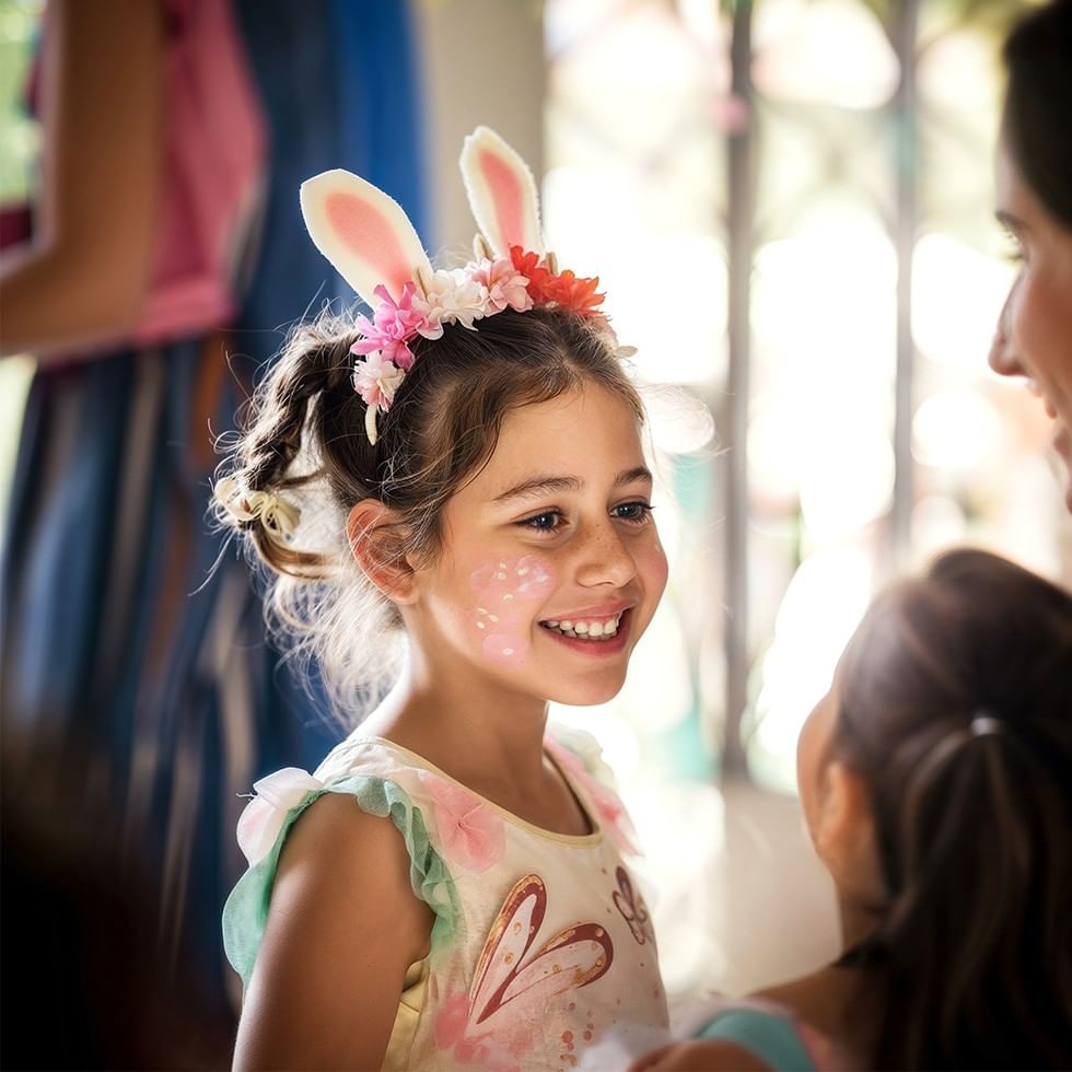 Bambina sorridente con orecchie di coniglio e fiori sulla testa.