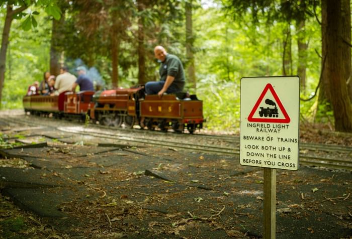 Miniature train with passengers on a track, accompanied by a warning sign for Ingfield Light Railway.