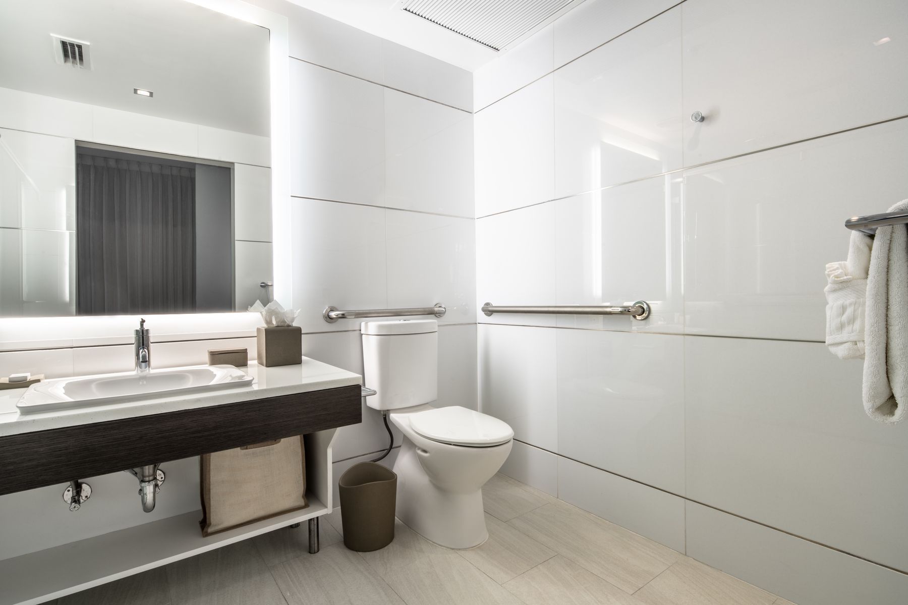 A clean, modern bathroom with a toilet, sink, and grab bars.