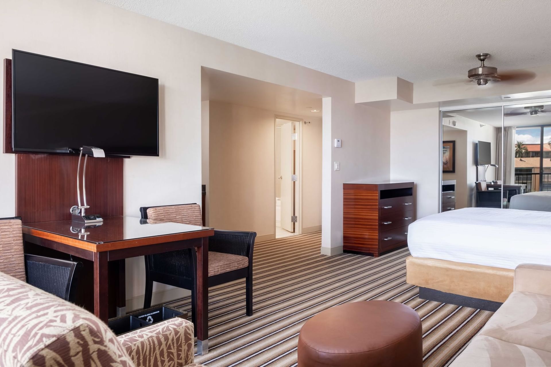 A wide view of a hotel room with a desk, TV, bed, and sofa.