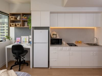 Compact kitchen with white cabinets, fridge, microwave, sink, and desk at UniLodge Brisbane City.