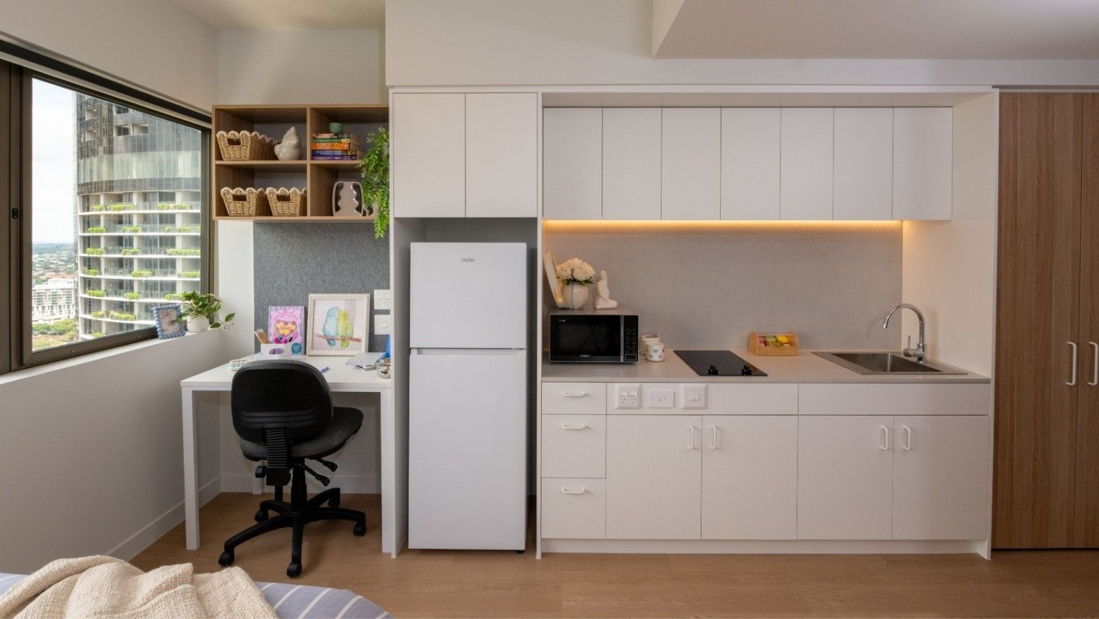 Compact kitchen with white cabinets, fridge, microwave, sink, and desk at UniLodge Brisbane City.