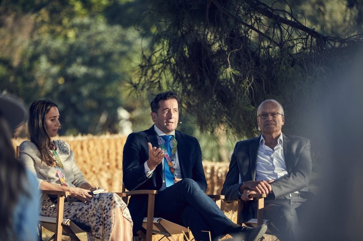 Three panelists seated outdoors, with the central male speaker passionately addressing the audience at Marbella Club