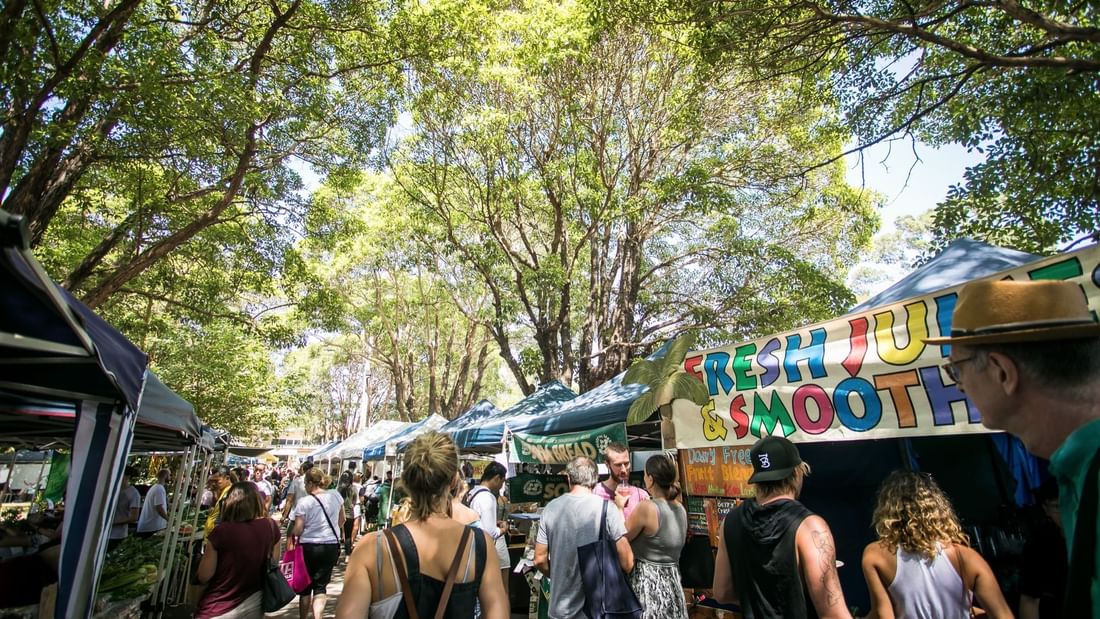 Crowds browsing stalls under shady trees at lively Marrickville Market near Novotel Sydney International Airport