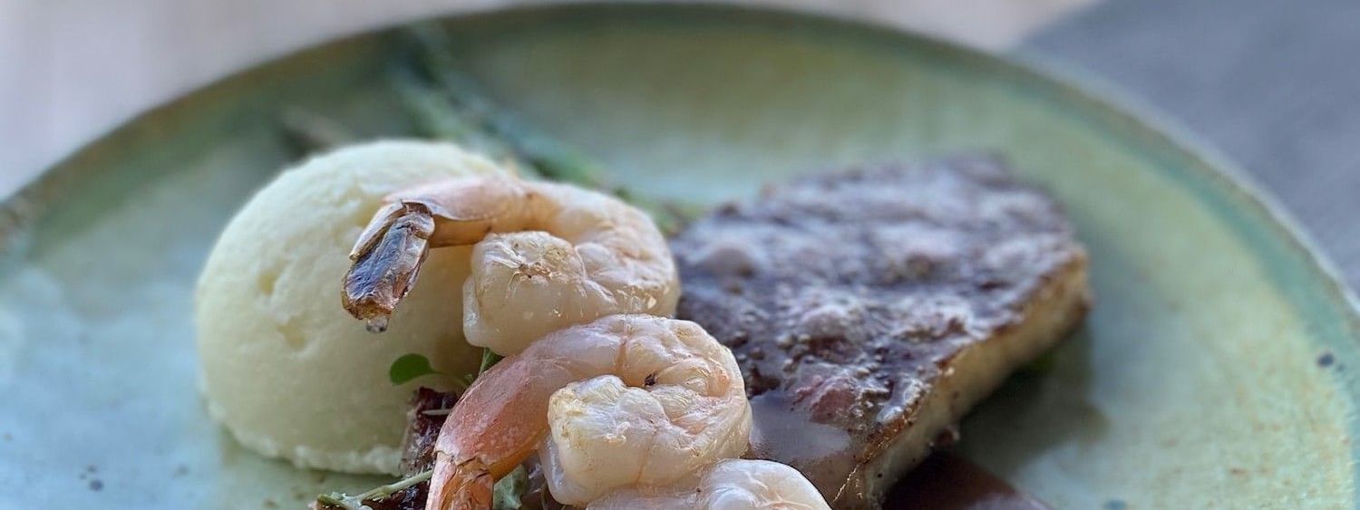 Seared steak topped with shrimp, mashed potatoes under a soft focus in Edgewater Grill at Warwick Paradise Island Bahamas