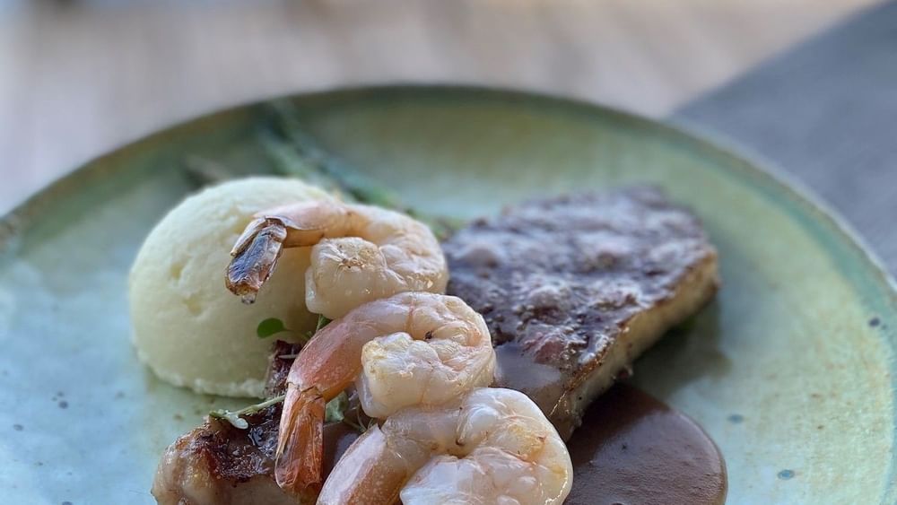 Seared steak topped with shrimp, mashed potatoes under a soft focus in Edgewater Grill at Warwick Paradise Island Bahamas