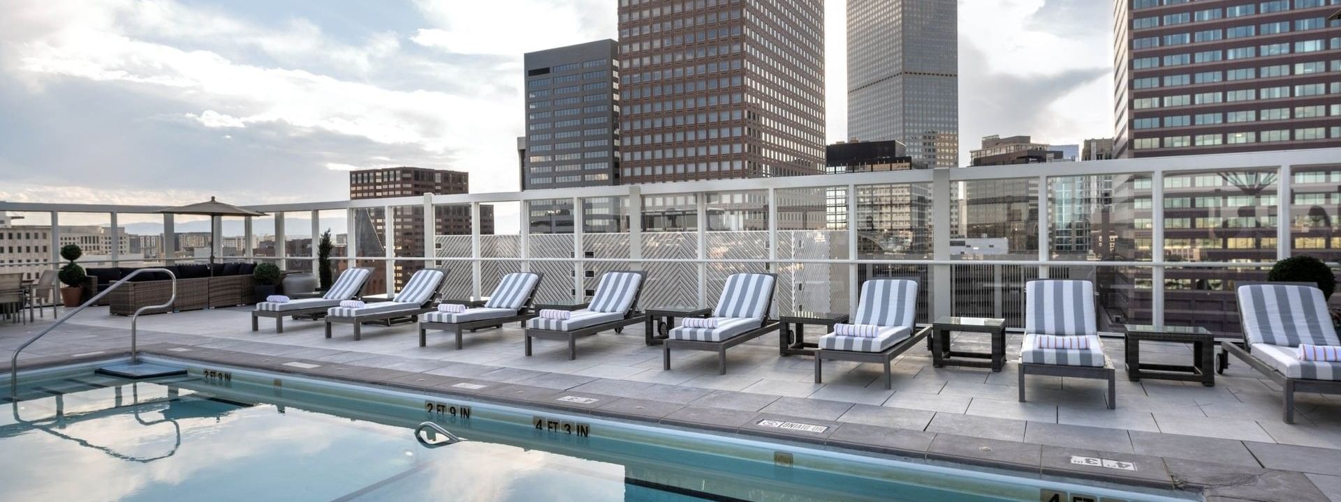 Rooftop pool with loungers by a glass fence under a sky with city buildings at Warwick Denver