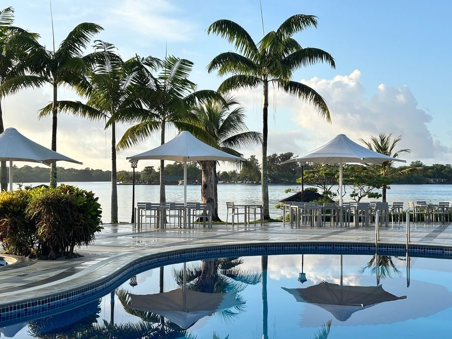 A pool with surrounding palm trees and dining area at Warwick Le Lagon Vanuatu.
