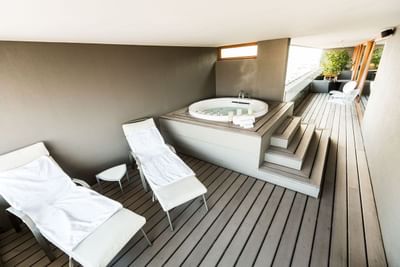 Jacuzzi junto a reposeras blancas bajo techo en deck de madera con baranda de vidrio en NOI Vitacura