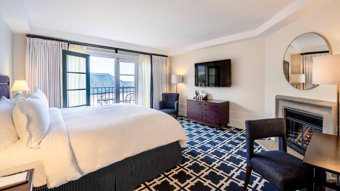 TV, dresser, and seating area by the cozy bed in Courtyard Deluxe Fireplace King at El Prado Hotel