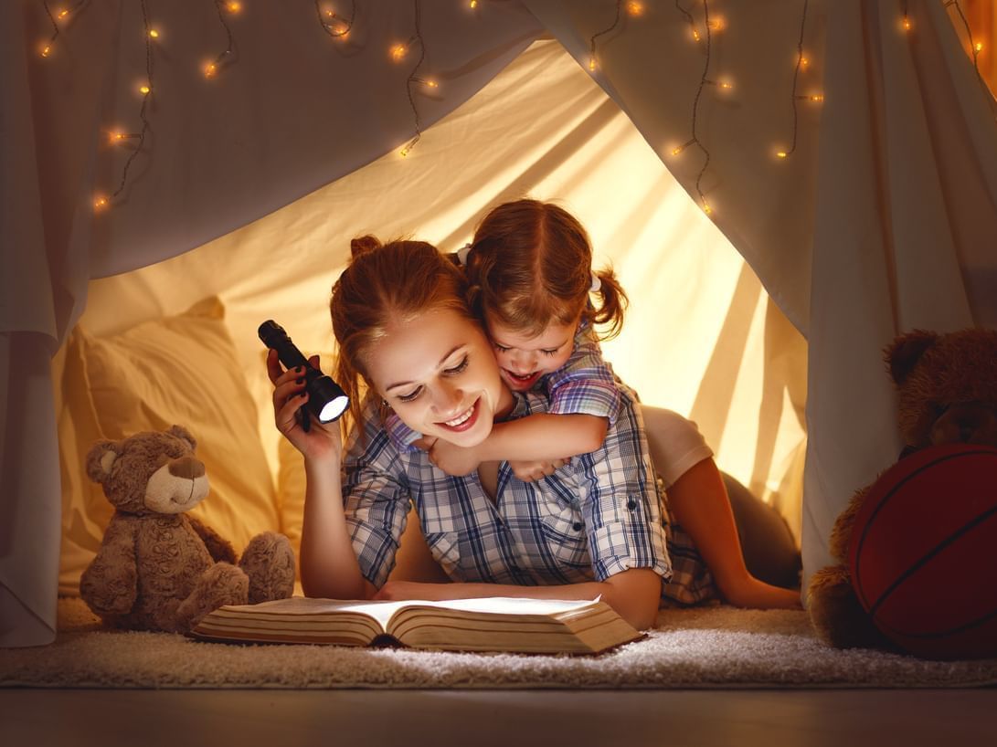 Mother & child with book & flashlight on a bed at Grand Coloane