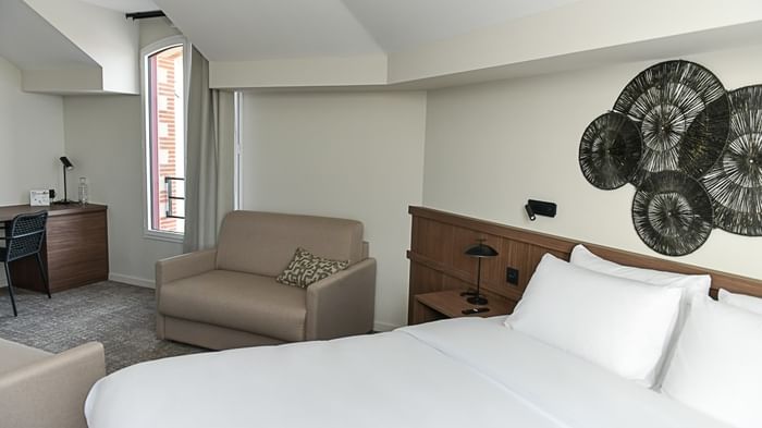 Chambre moderne avec lit blanc et fauteuil au Hôtel Rivella.