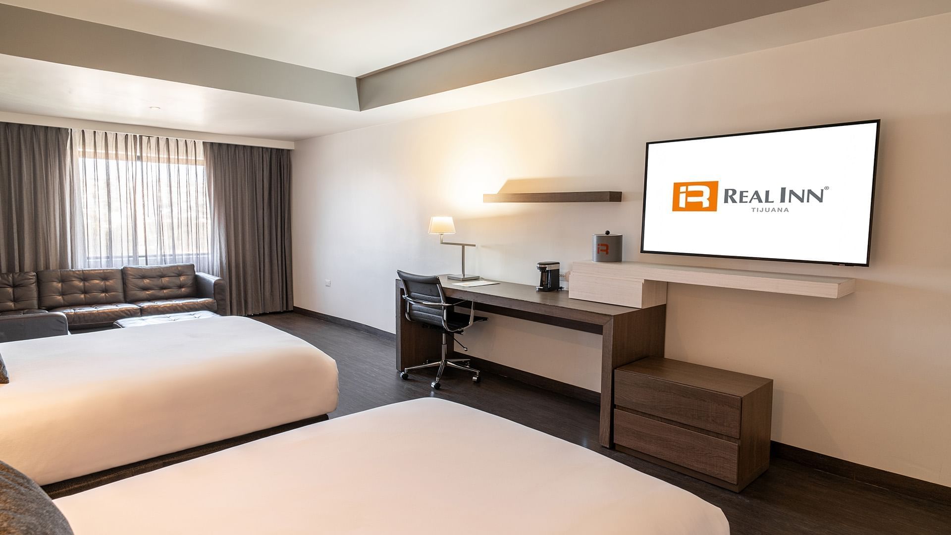 Wall-mounted TV and work desk facing the beds in Two Double Junior Suite with wooden floors at Real Inn Tijuana