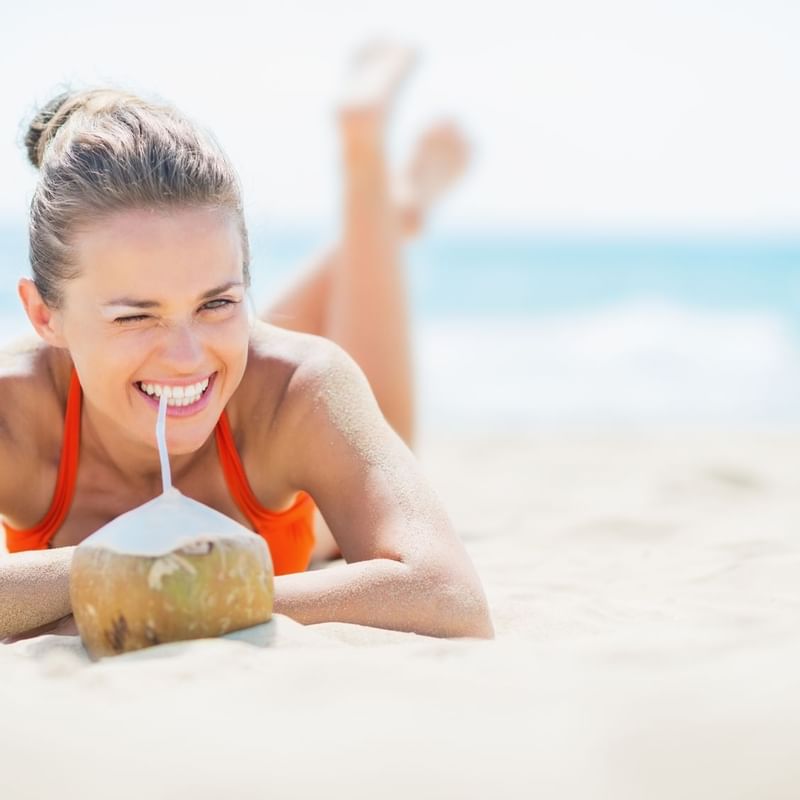 A girl laying on the beach, drinking coconut at TokaToka Resort