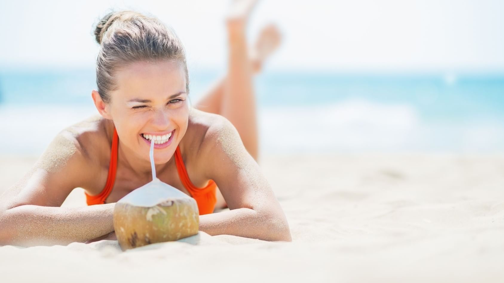 A girl laying on the beach, drinking coconut at TokaToka Resort