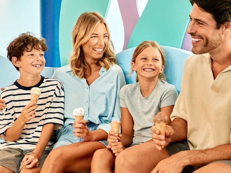 Familie genießt gemeinsam Eis auf einer bunten Bank, umgeben von farbenfrohen Wänden.