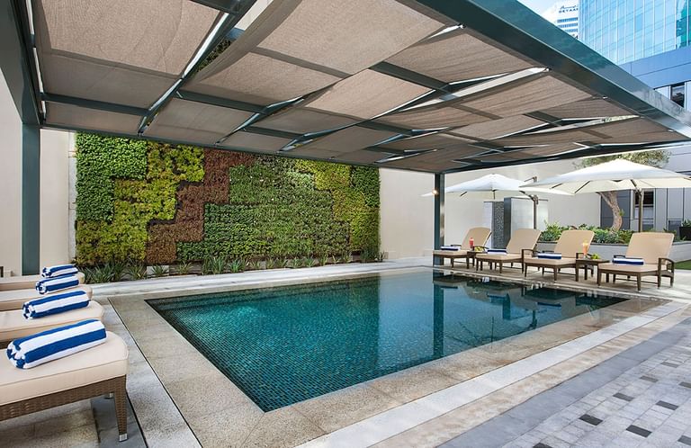 Modern pool with loungers, umbrellas, and a green wall under a pergola at DAMAC Maison Cour Jardin