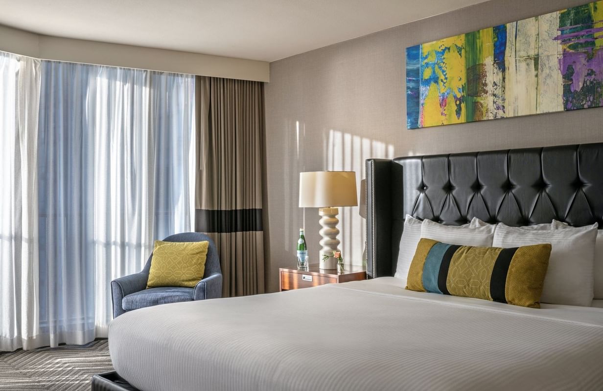 Emerald Suite with an armchair by a window and a tufted bed under art at Warwick Seattle