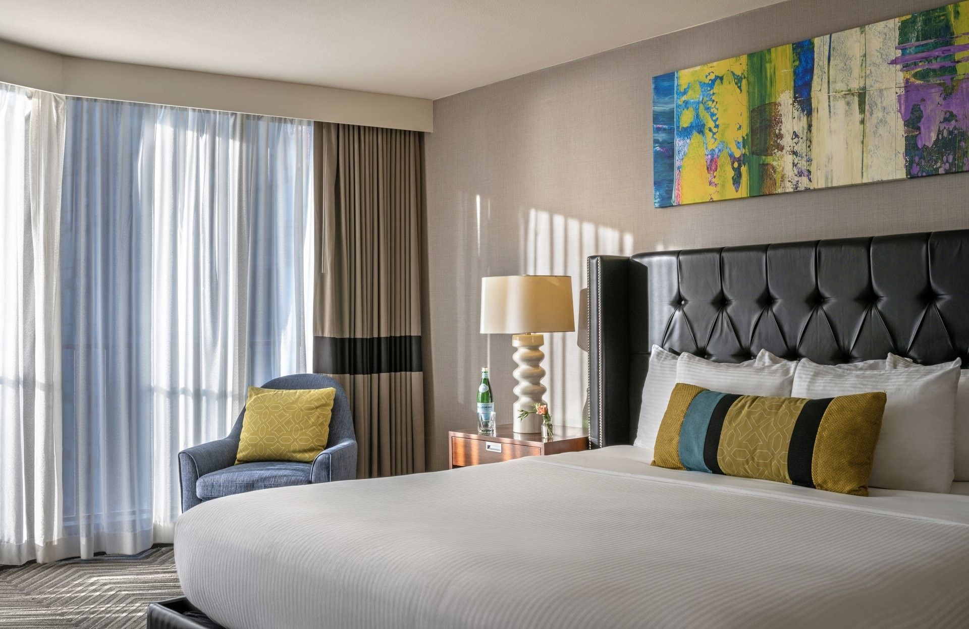 Emerald Suite with an armchair by a window and a tufted bed under art at Warwick Seattle