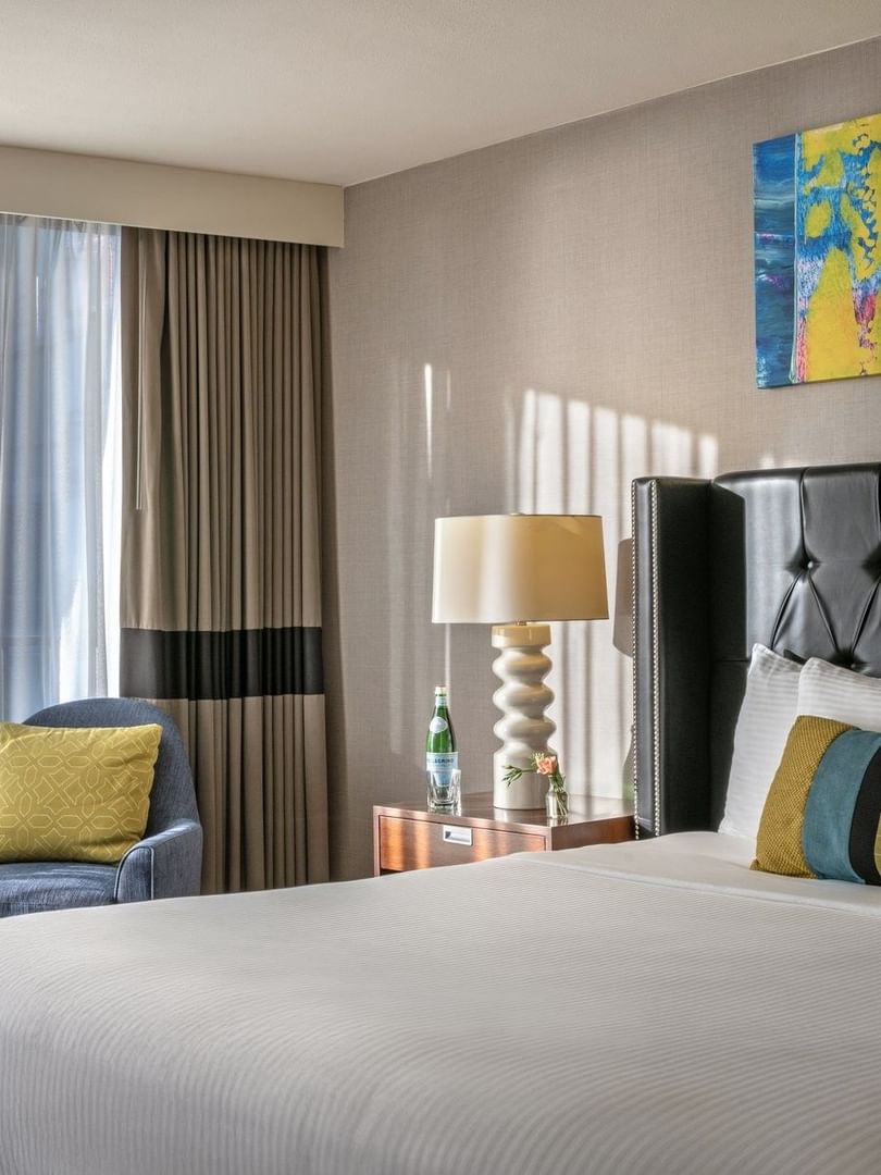 Emerald Suite with an armchair by a window and a tufted bed under art at Warwick Seattle