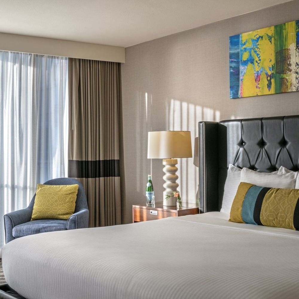 Emerald Suite with an armchair by a window and a tufted bed under art at Warwick Seattle