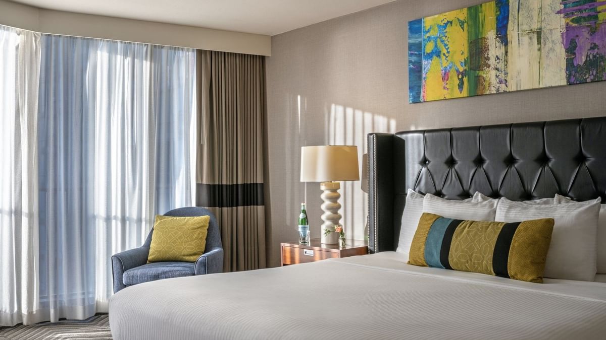 Emerald Suite with an armchair by a window and a tufted bed under art at Warwick Seattle