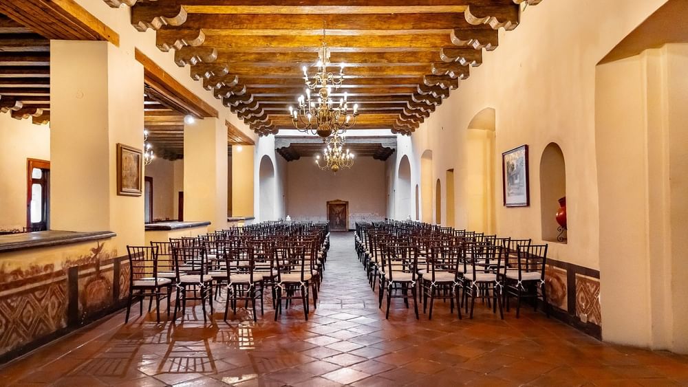 La Concepción event hall with wood beam ceilings, chandeliers, and rows of dark wooden chairs at Quinta Real Puebla